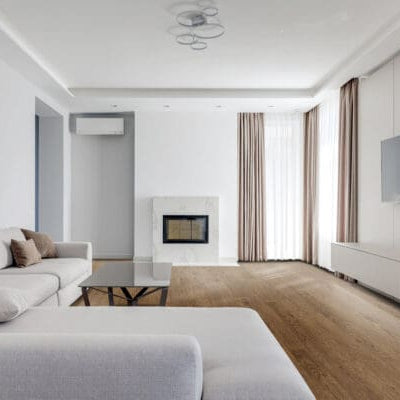 Modern living room with white furniture, a fireplace, and a television. Neutral mid tone brown hardwood floor featuring Coastline - Milford Sound luxury vinyl plank floor