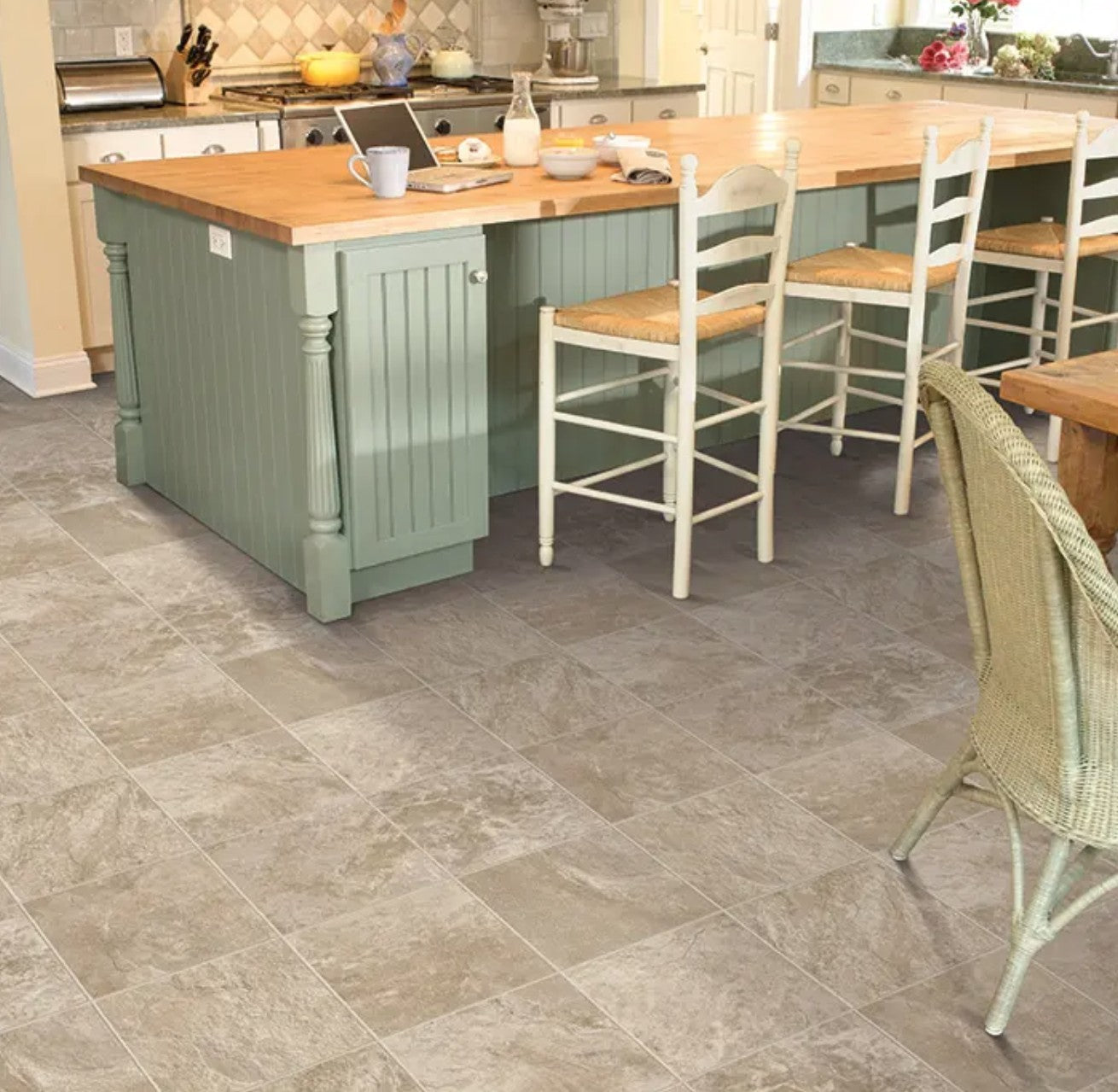 Kitchen with a green island and wooden chairs on a gray tiled floor. Mannington sheet vinyl Muir's Point Riverstone Blend.