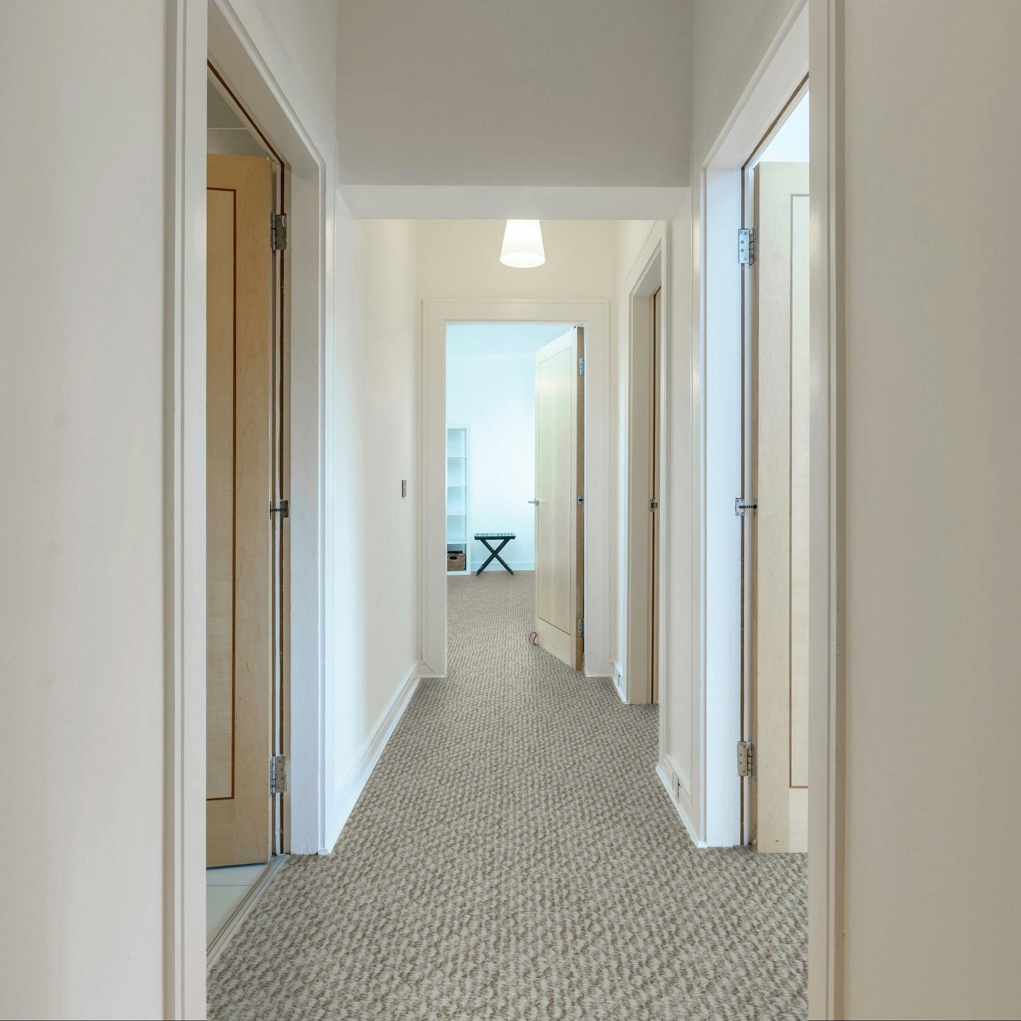 Long hallway with carpeted floor and white walls, leading to a room with a desk and window. Beaulieu carpet Nostalgia made in Canada.