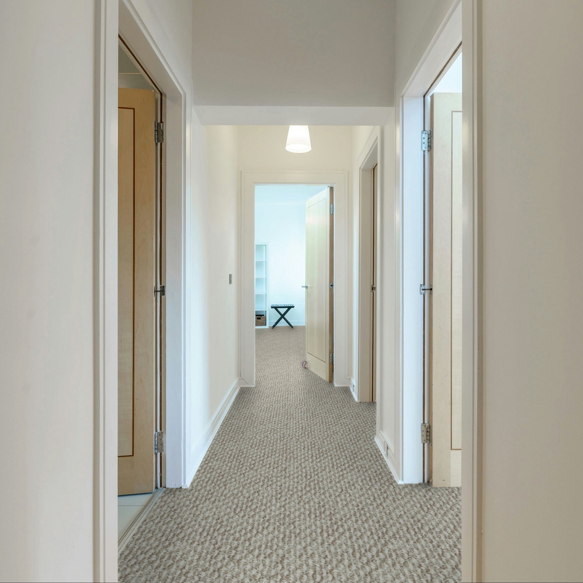 Long hallway with carpeted floor and white walls, leading to a room with a desk and window. Beaulieu carpet Nostalgia made in Canada.