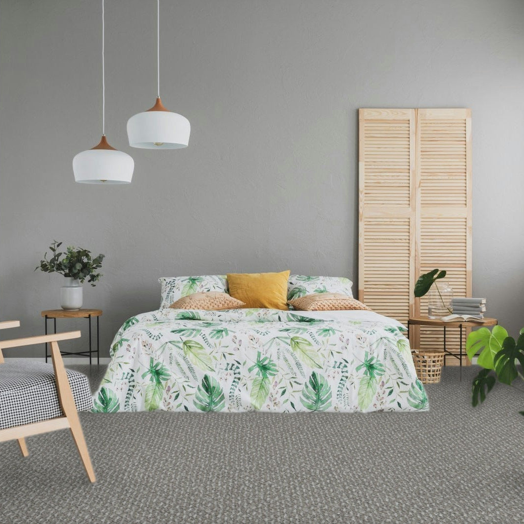 Modern bedroom with a bed featuring a green leaf-patterned comforter, a chair, and plants. Beaulieu Nostalgia Norfolk Grey carpet made in Canada.